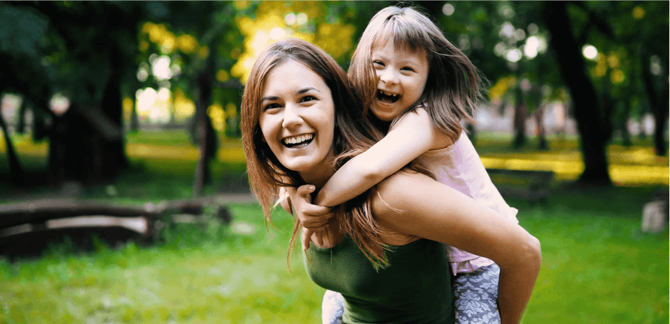 Woman giving a young girl a piggyback in a park