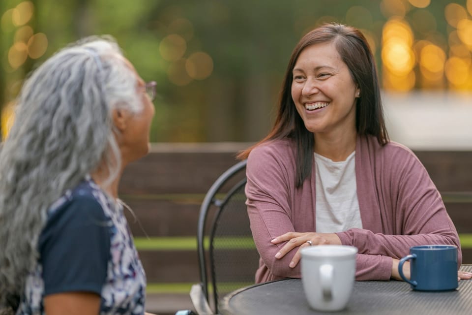 Two women smiling and sharing a hot drink outdoors