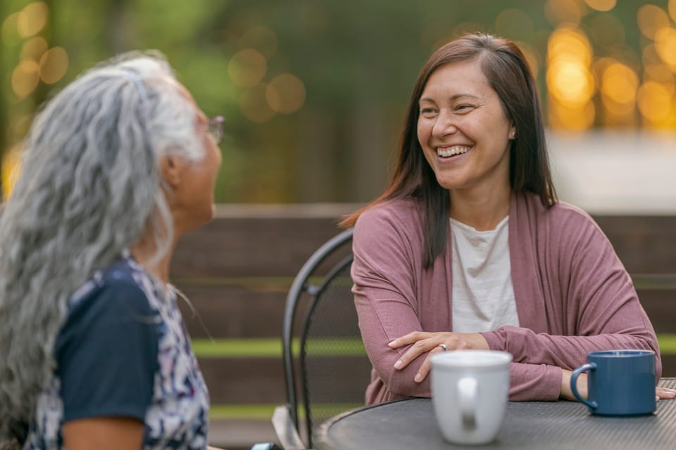 A younger and an older woman talking over coffee outside